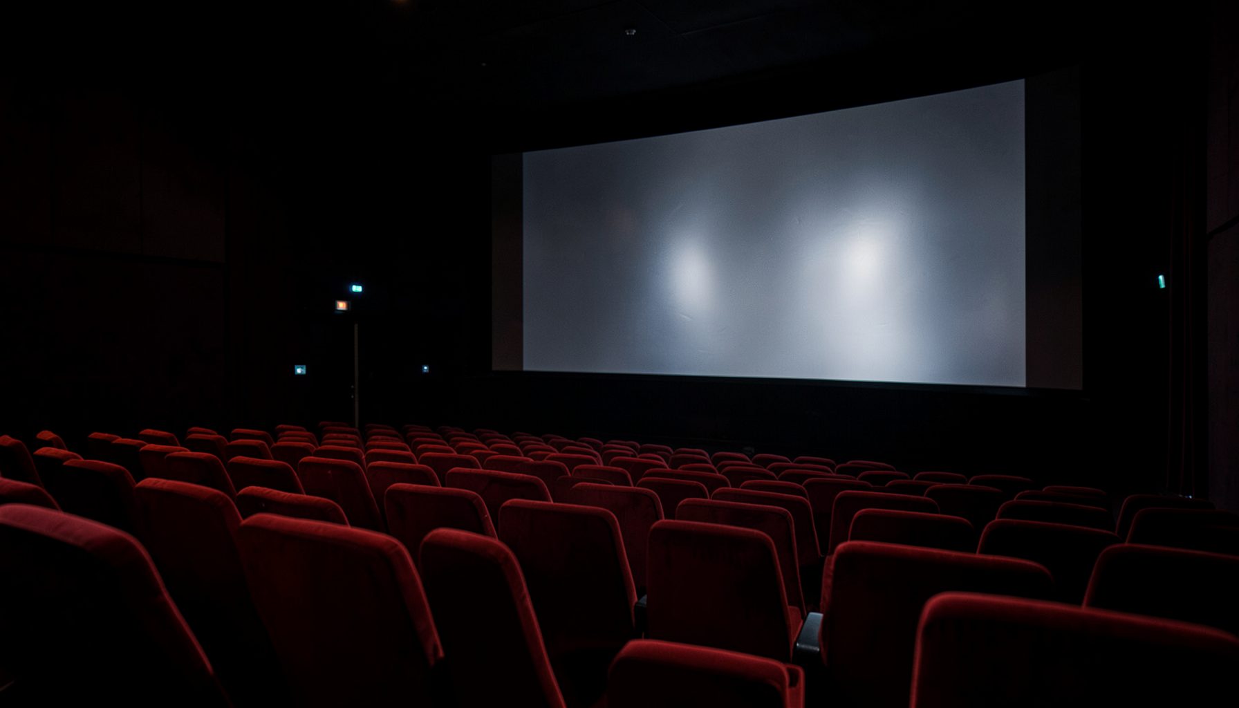 A darkened cinema auditorium with deep red velvet seats and a glowing silver screen, moody and atmospheric