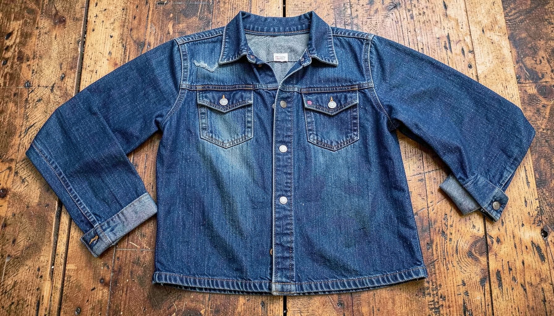 A denim-on-denim outfit laid flat on a rustic wooden surface, rich indigo blues and warm wood tones