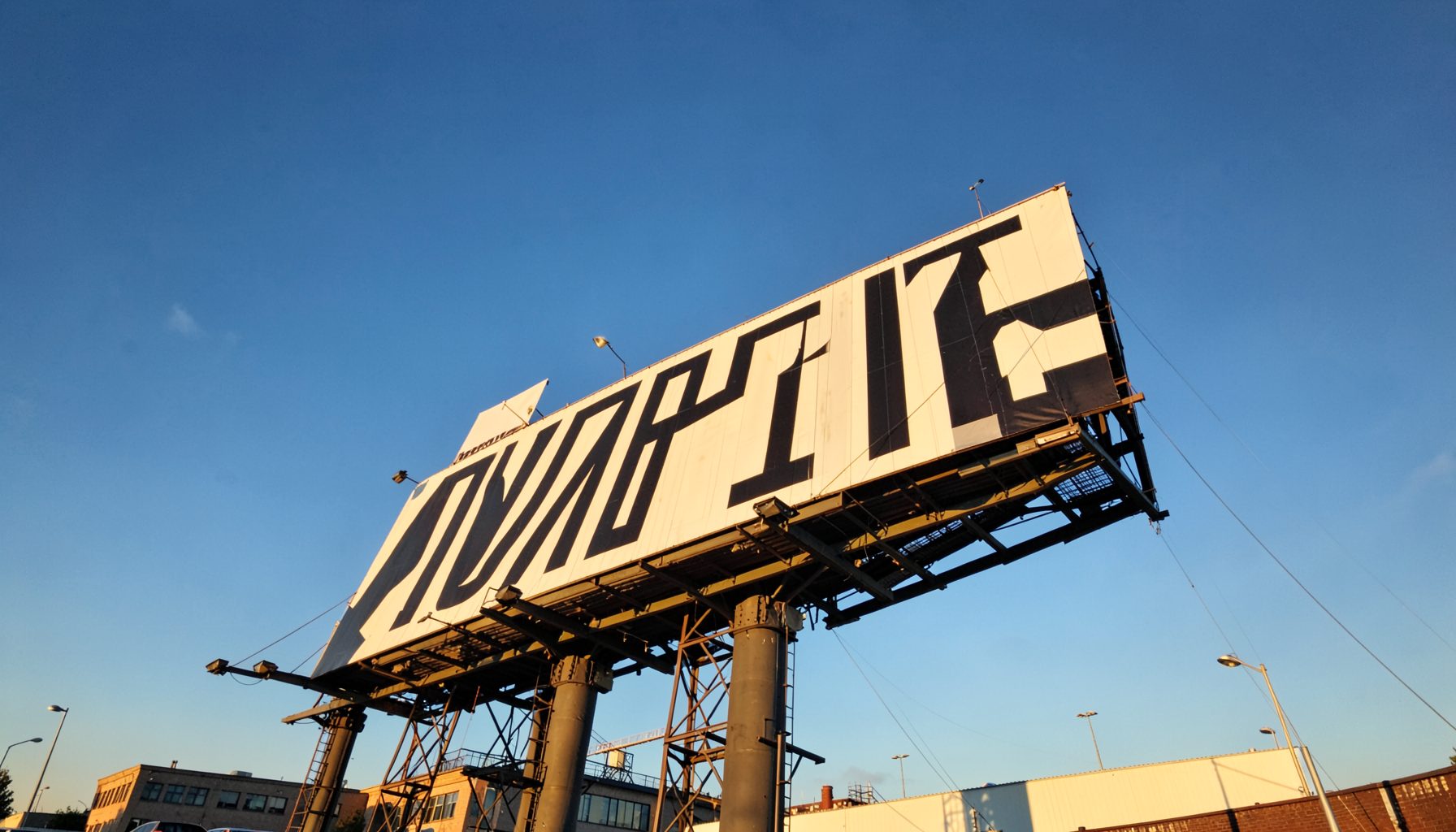 A large billboard with bold lettering against a blue sky, seen from a low angle, warm afternoon light