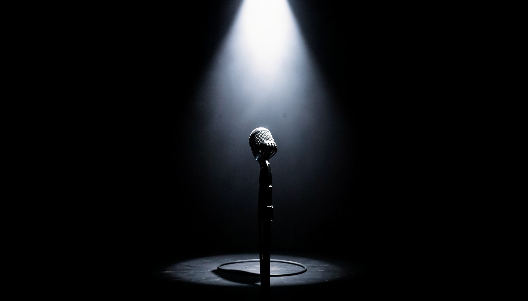 A microphone on a dark stage with a single spotlight, dramatic contrast of bright white light against deep black