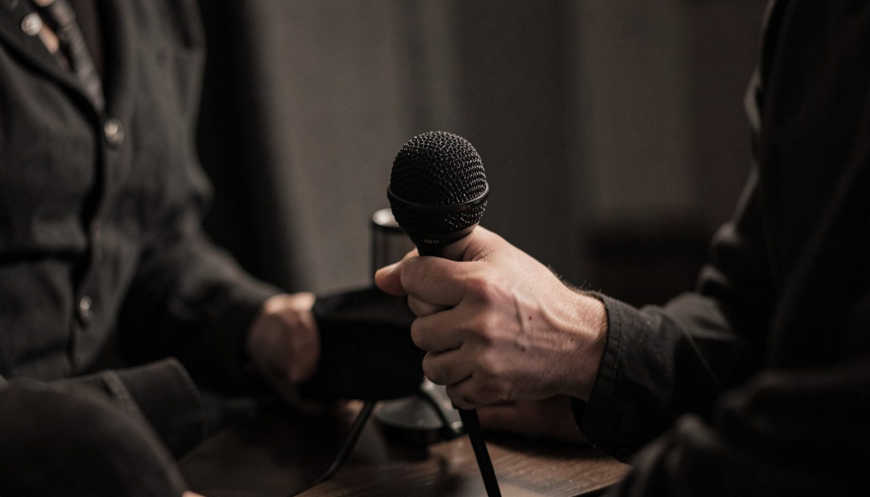 A pair of hands holding a microphone during an intimate charcoal-toned interview setting