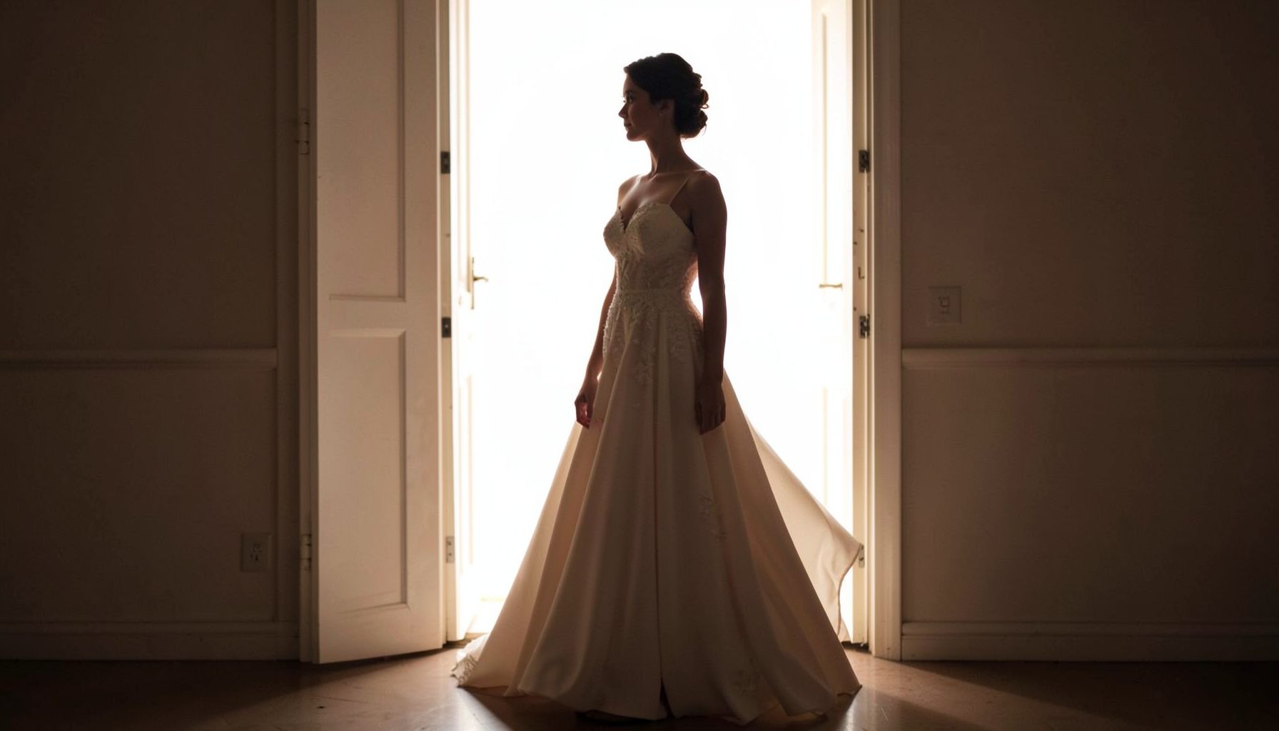 A single figure in a flowing evening dress silhouetted against a bright doorway, soft cream and blush tones