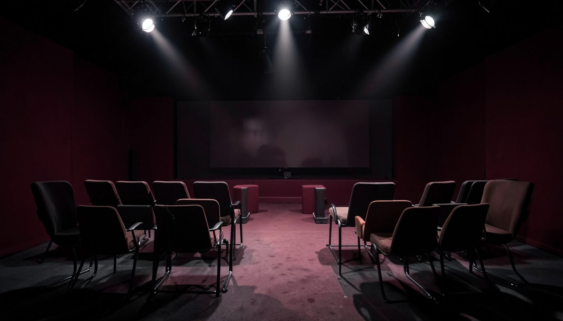 A television studio set with empty chairs and dramatic overhead lighting, deep burgundy and charcoal tones