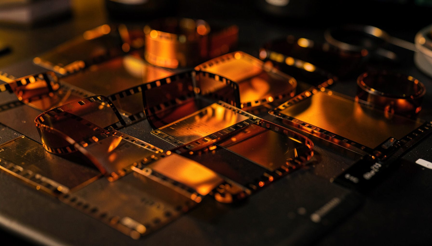 Reels of 35mm film stock in warm amber and deep orange tones, arranged on a dark editing bench