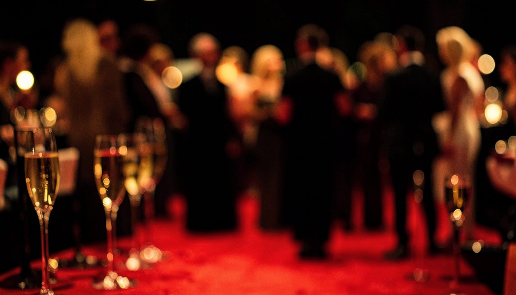 Soft-focus scene of a glamorous red-carpet after-party with warm golden lighting, champagne glasses, and blurred elegant silhouettes against a dark backdrop